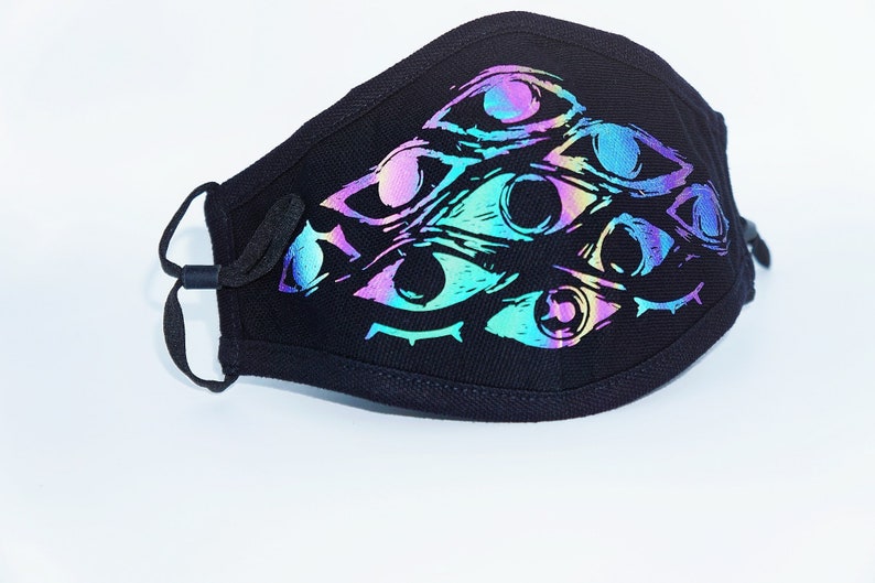 May include: Black face mask featuring a design of multiple iridescent eyes. The eyes have a color gradient of purple, blue, and green. The mask has adjustable ear loops for a comfortable fit.