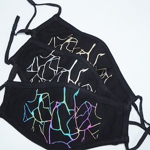 Könnte beinhalten: Drei schwarze Gesichtsmasken mit verschiedenen schillernden Designs. Die Designs bestehen aus einem dünnen, reflektierenden Material, das einen schimmernden Effekt erzeugt.