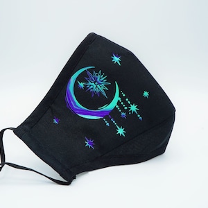 May include: Black face mask with a crescent moon and stars design in shades of blue and green.