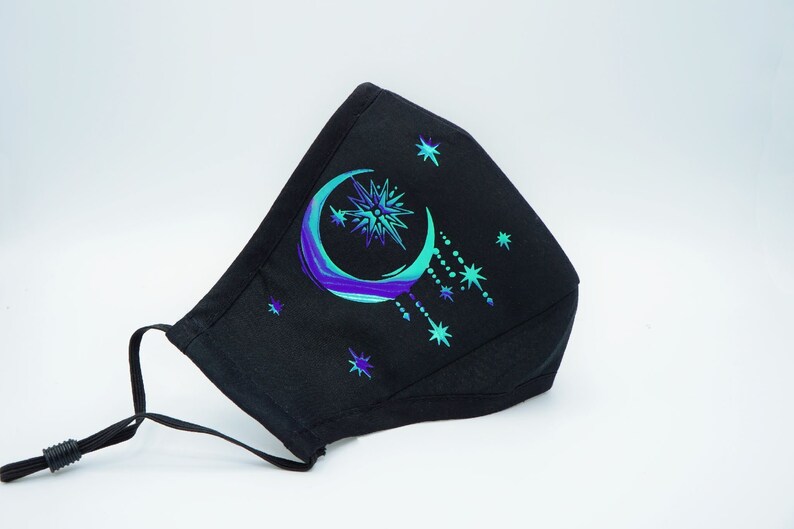 May include: Black face mask with a crescent moon and stars design in shades of blue and green.