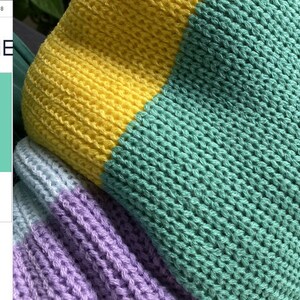 May include: A close-up of a knitted fabric with stripes of yellow, light blue, purple, and green. The fabric is textured and has a loose weave.