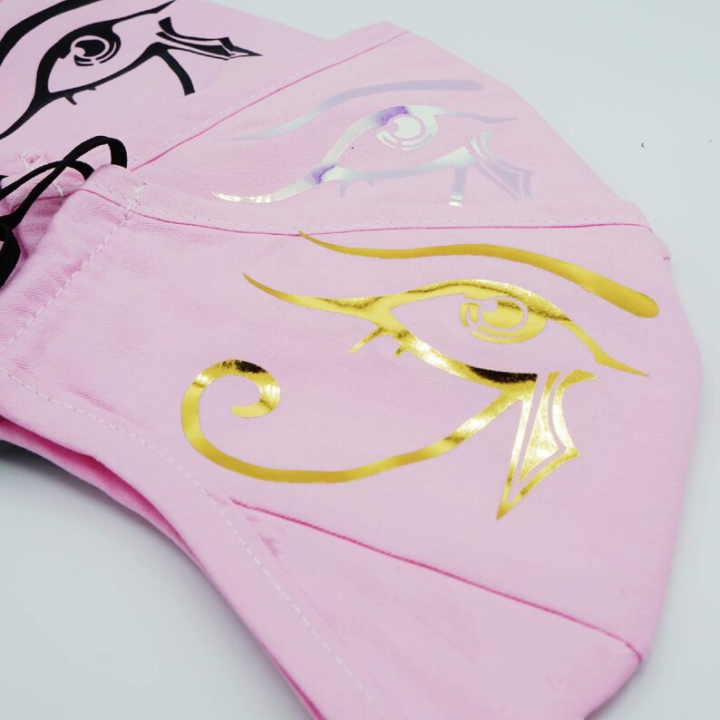 May include: Pink fabric face mask with a gold eye of Horus design.