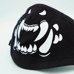 Puede incluir: Máscara facial negra con un gráfico blanco de los dientes y colmillos de un animal que gruñe.