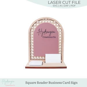 May include: A wooden business card sign with a square reader slot and a business card holder. The sign has a pink centre with the text "Hydrangea Creations Co." and a decorative wooden arch. The top text reads "LASER CUT FILE".