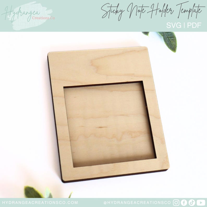 May include: A wooden sticky note holder template. The template is a square with a smaller square cut out in the center. The template is light brown in color.
