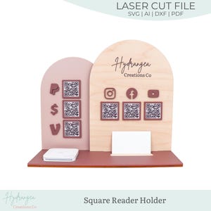 Op de afbeelding: Een houten Square Reader-houder met een lichtroze en natuurlijk houten afwerking. Het heeft QR-codes, social media-pictogrammen en de tekst "Hydrangea Creations Co." De houder heeft een sleuf voor visitekaartjes en ruimte voor een Square-reader.