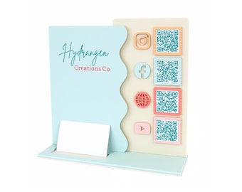 Pode incluir: Um porta-cartões de visita azul claro com uma ranhura para cartões branca. O porta-cartões tem um design decorativo com uma borda ondulada e um painel com ícones de mídia social e códigos QR. O painel tem um fundo marrom claro com acentos rosa, vermelho e azul. O texto "Hydrangea Creations Co" está impresso no porta-cartões.