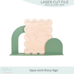 May include: A wooden sign with a wavy edge, set within a green arch-shaped frame. The sign is light-coloured wood, and the frame is a muted green. Text at the top reads "LASER CUT FILE". The sign is labelled "Open Arch Wavy Sign".
