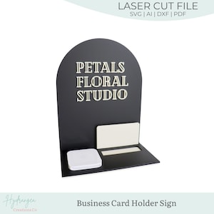 May include: Black business card holder sign with the text "PETALS FLORAL STUDIO" in a serif font. The sign has a curved top and a shelf for business cards and a small square object. The words "LASER CUT FILE" are at the top.