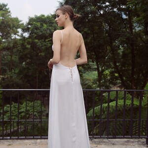 K&ouml;nnte beinhalten: Ein wei&szlig;es Maxikleid mit tiefem R&uuml;cken und einem Schn&uuml;rdetail. Das Kleid ist flie&szlig;end und hat eine lockere Passform.