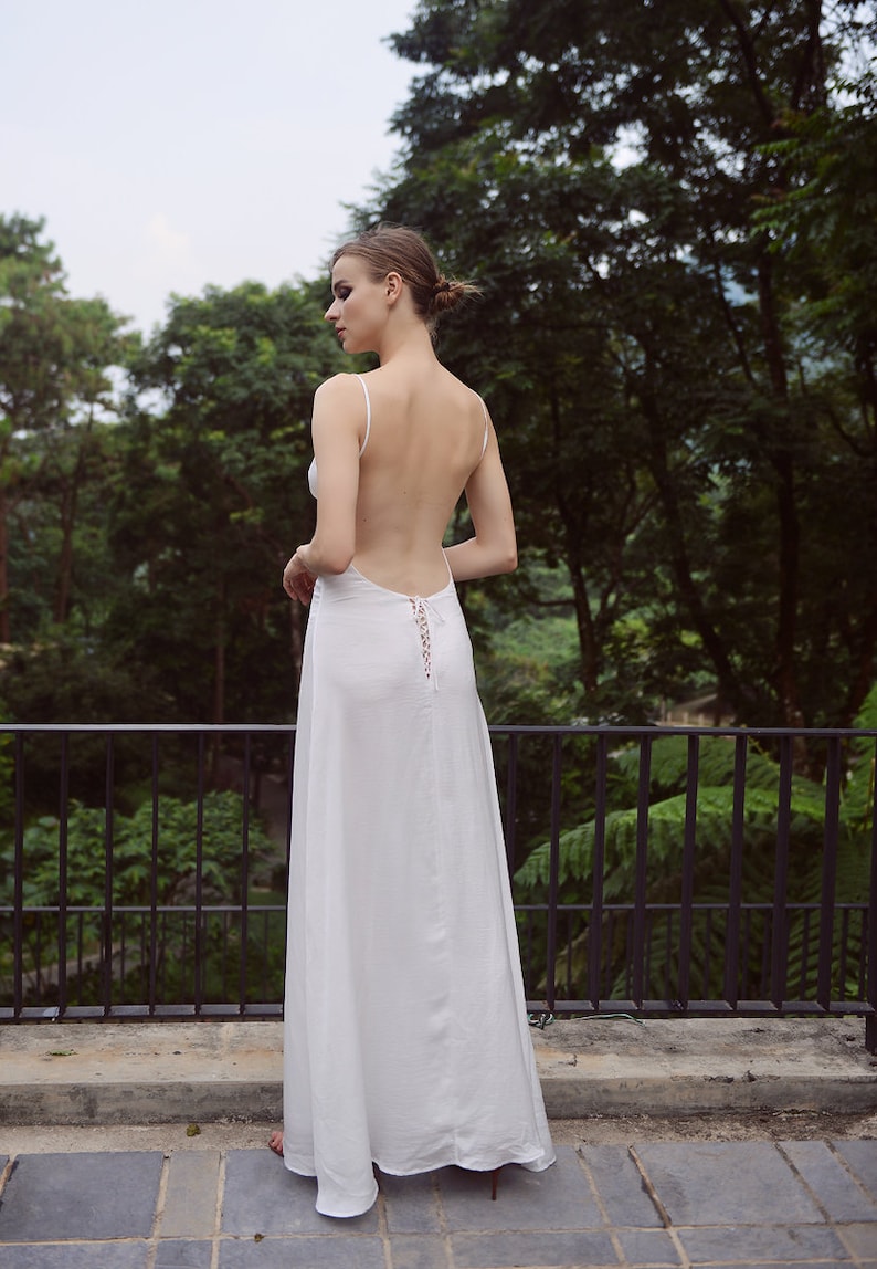 K&ouml;nnte beinhalten: Ein wei&szlig;es Maxikleid mit tiefem R&uuml;cken und einem Schn&uuml;rdetail. Das Kleid ist flie&szlig;end und hat eine lockere Passform.