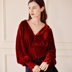 May include: A red velvet blouse with a V-neckline, long sleeves, and a button-up front. The blouse has a fitted bodice and a gathered waist.