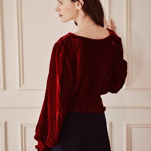 May include: A red velvet blouse with long sleeves and a gathered waistline, paired with a black plaid skirt.