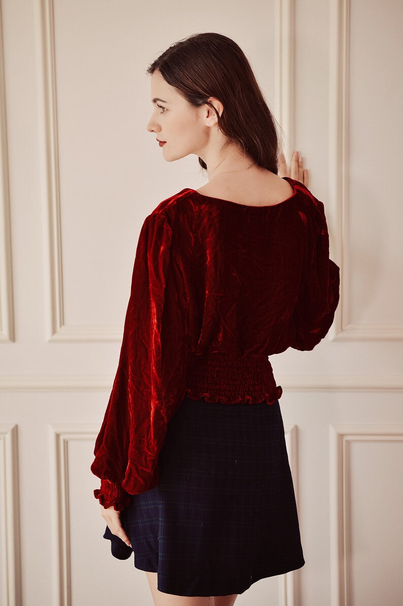 May include: A red velvet blouse with long sleeves and a gathered waistline, paired with a black plaid skirt.