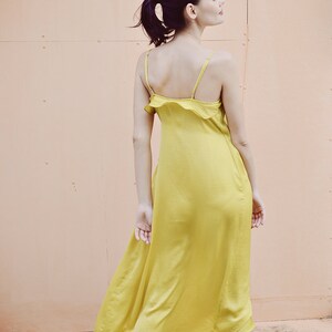 May include: A yellow satin midi dress with spaghetti straps and a ruffled neckline. The dress is a vibrant shade of yellow and has a flowing, elegant silhouette. The dress is knee-length and appears to be made of a lightweight fabric.
