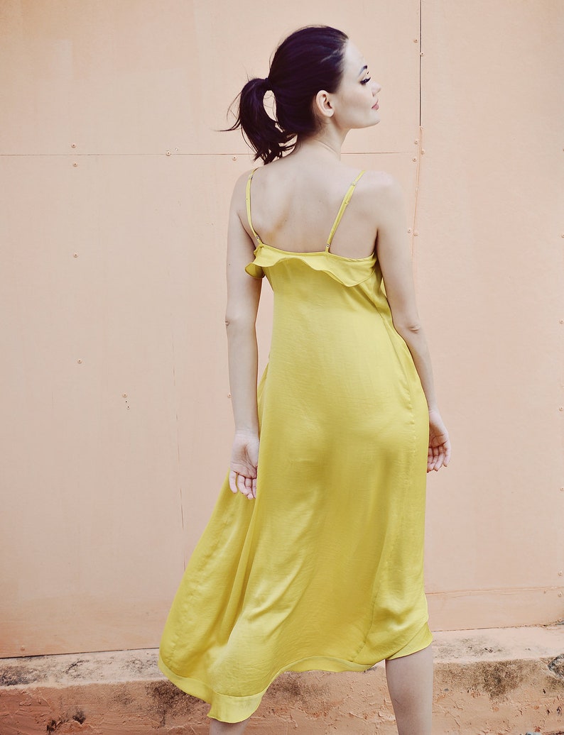 May include: A yellow satin midi dress with spaghetti straps and a ruffled neckline. The dress is a vibrant shade of yellow and has a flowing, elegant silhouette. The dress is knee-length and appears to be made of a lightweight fabric.