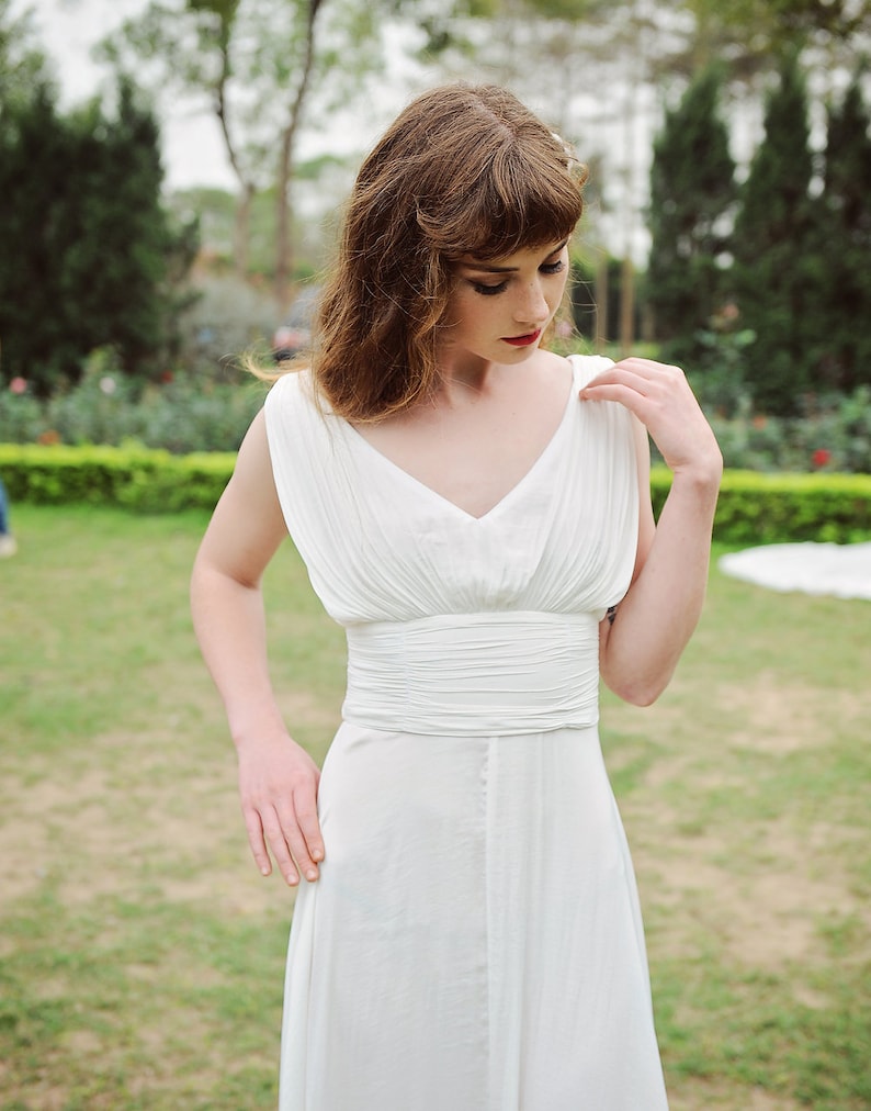 May include: A woman wearing a white, sleeveless dress with a fitted bodice and a flowing skirt. The dress has a V-neckline and a simple design.