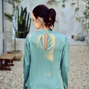 May include: A teal satin blouse with a keyhole back and long sleeves.