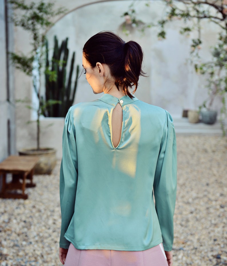 May include: A teal satin blouse with a keyhole back and long sleeves.