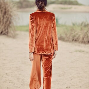 May include: A person wearing a rust-colored velvet pajama set with long sleeves and wide-leg pants. The person is walking on a sandy beach.