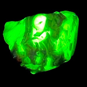 May include: A bright green, irregularly shaped, translucent stone with a smooth surface. The stone is illuminated from the inside, creating a glowing effect.