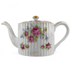 Peut inclure: Théière blanche avec une bordure dorée et un motif floral de roses roses. La théière a un design côtelé et un bouton doré sur le couvercle.