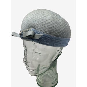 May include: A light blue felt hat with a small bow and a decorative pin. The hat has a textured surface and a blue ribbon around the brim.