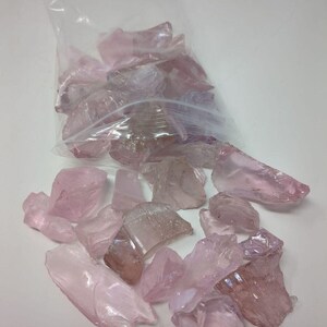 May include: A bag of pink iridescent glass shards. The shards are various sizes and shapes, with some being long and thin, while others are short and chunky.