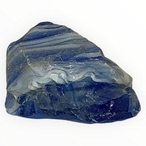 Puede incluir: Una piedra natural en bruto con una apariencia en capas. La piedra presenta tonos de azul y gris, con una mezcla de tonos claros y oscuros. La superficie tiene una apariencia texturizada e irregular, lo que sugiere una formación geológica. La piedra está sobre un fondo blanco.