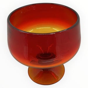 May include: A vintage, amber-colored glass goblet with a rounded bowl and a short stem. The glass transitions from a deep red at the top to a golden hue at the base. The goblet is likely used for serving beverages.