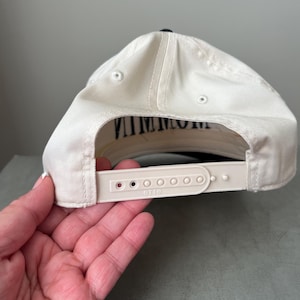 Puede incluir: Gorra de b&eacute;isbol color crema con visera negra y la palabra "VINTAGE" impresa en negro en la parte inferior de la visera. La gorra tiene una correa ajustable blanca con la marca "OTTO" impresa.