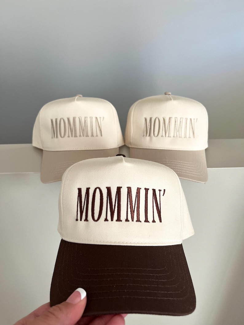 Puede incluir: Tres gorras de b&eacute;isbol con la palabra "MOMMIN'" bordada en la parte delantera. Las gorras tienen un panel frontal blanco y una visera marr&oacute;n. El texto est&aacute; bordado en marr&oacute;n a juego.