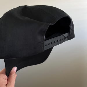 Pode incluir: Um bon&eacute; de beisebol preto com uma correia ajust&aacute;vel preta. O bon&eacute; &eacute; feito de um tecido de algod&atilde;o macio.