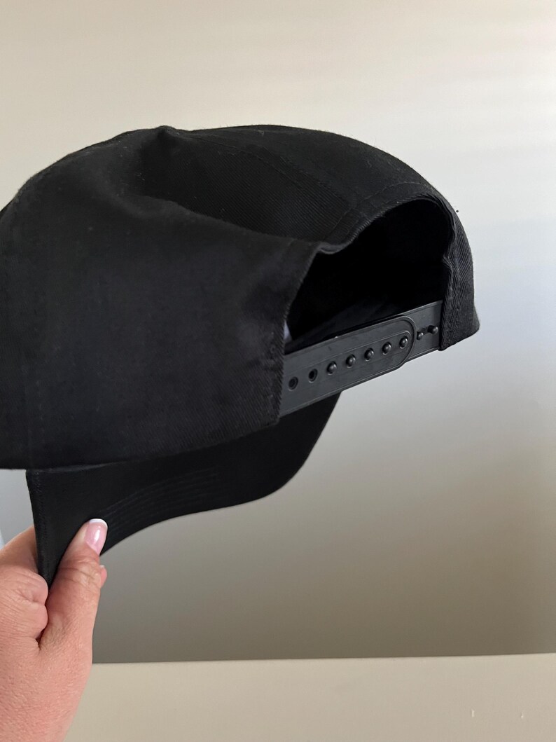 Pode incluir: Um bon&eacute; de beisebol preto com uma correia ajust&aacute;vel preta. O bon&eacute; &eacute; feito de um tecido de algod&atilde;o macio.
