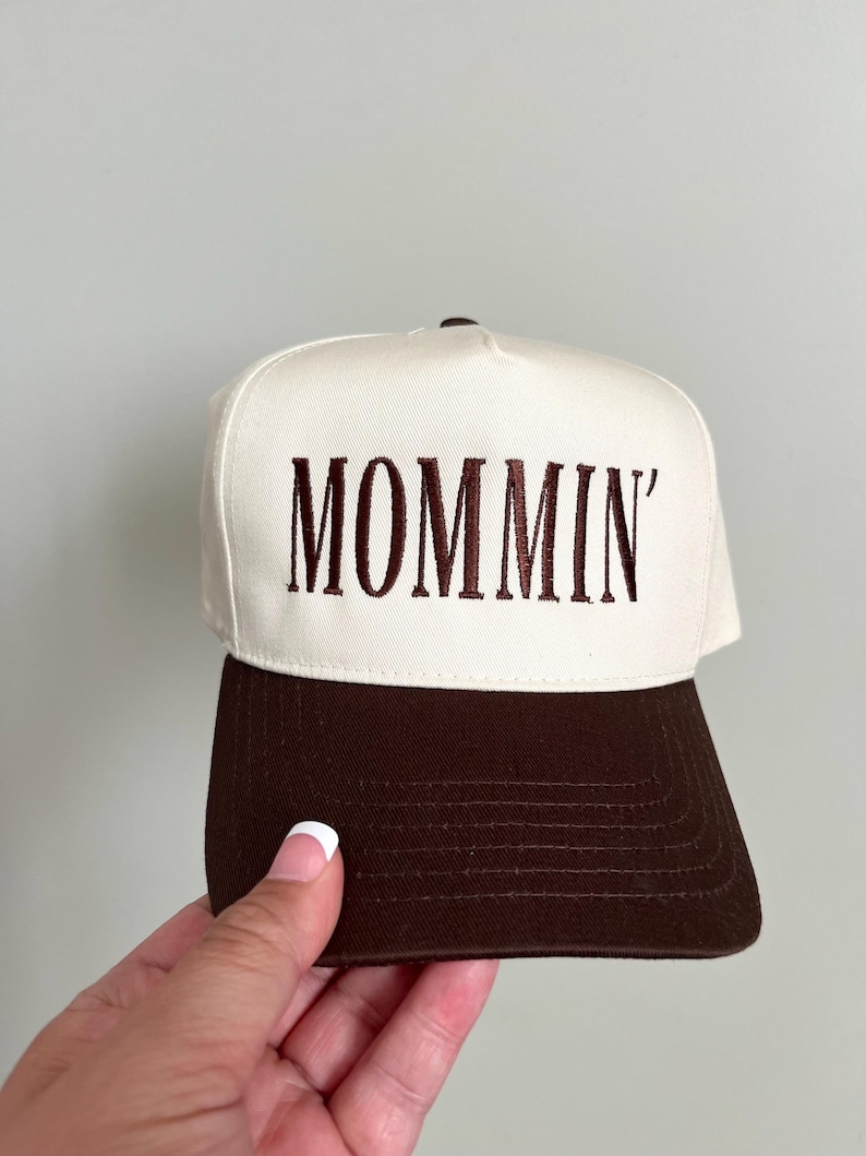 Puede incluir: Gorra de b&eacute;isbol con corona blanca y visera marr&oacute;n. La palabra "MOMMIN'" est&aacute; bordada en marr&oacute;n en la parte delantera. La gorra tiene un dise&ntilde;o cl&aacute;sico de seis paneles.