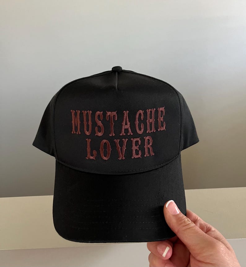 Pode incluir: Bon&eacute; de beisebol preto com uma frase bordada em vermelho "MUSTACHE LOVER" na frente.