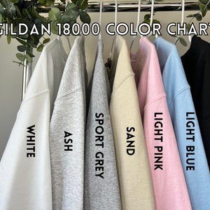 May include: Color chart for Gildan 18000 sweatshirts, showing the colors white, ash, sport grey, sand, light pink, light blue, and black.