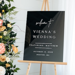 May include: Black acrylic wedding sign with white text. The sign reads "Welcome to Vienna's Wedding Featuring: Matthew October 14, 2025 Boston, MA". Shown size 18"x24" White Design Opaque Black Acrylic.