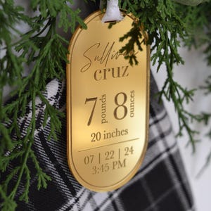 May include: Gold-coloured oval ornament with the text "Sullivan Cruz" and the baby's birth stats: 7 pounds, 8 ounces, 20 inches, 07 | 22 | 24 3:45 PM.
