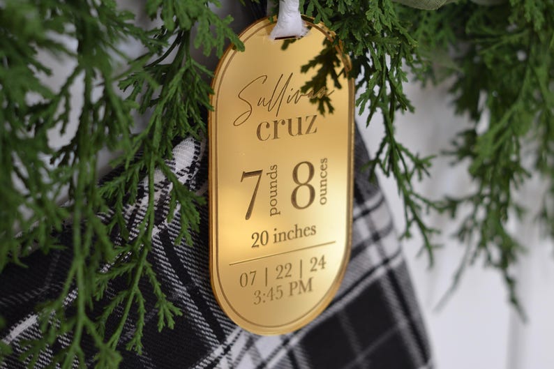 May include: Gold-coloured oval ornament with the text "Sullivan Cruz" and the baby's birth stats: 7 pounds, 8 ounces, 20 inches, 07 | 22 | 24 3:45 PM.
