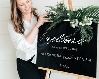 May include: Black welcome sign with white lettering on an easel. The sign reads "Welcome to our wedding Alexandra and Steven 3.5.2022".
