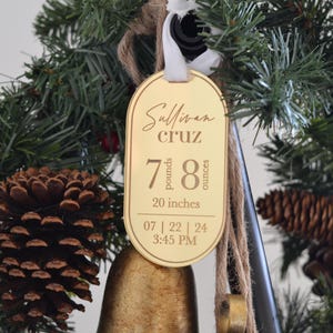 May include: A gold-coloured ornament with the name "Sullivan Cruz" and birth details: 7 pounds, 8 ounces, 20 inches, 07 | 22 | 24 3:45 PM. The ornament is hanging on a Christmas tree.