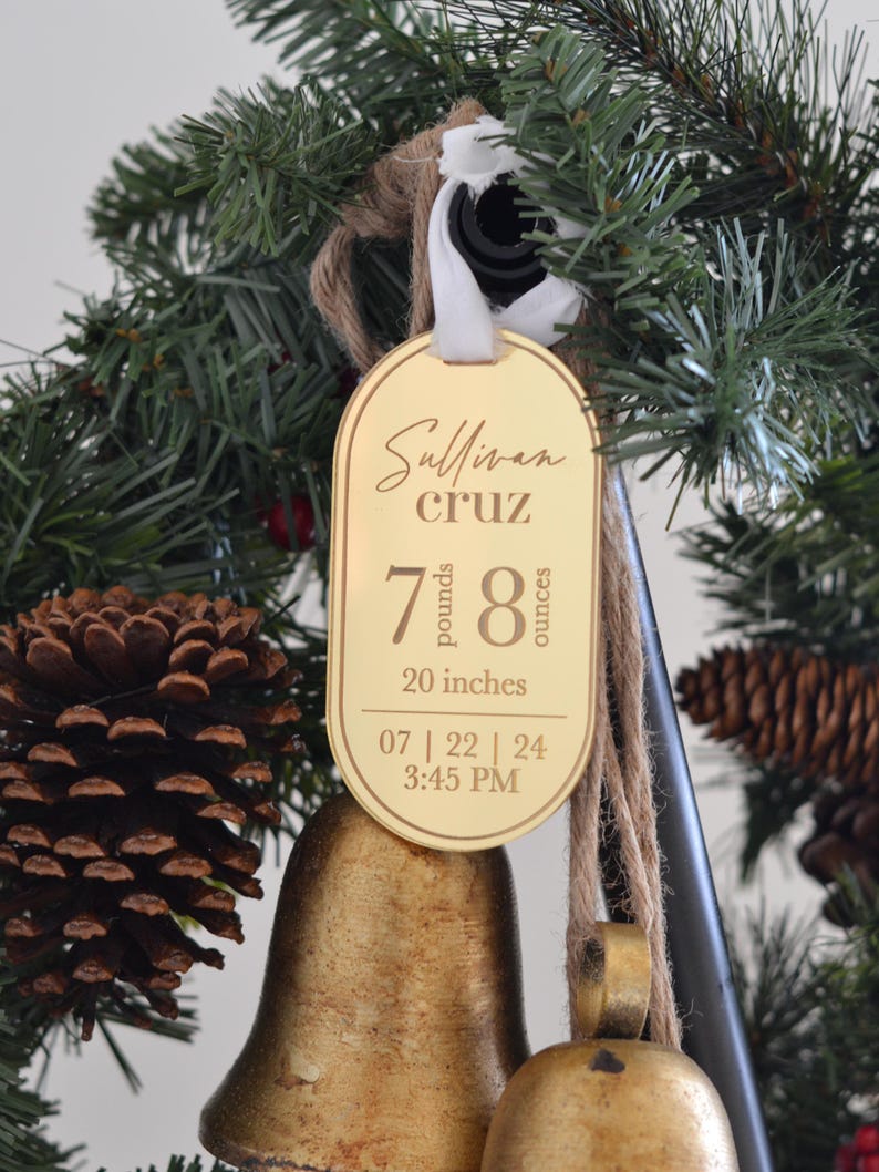 May include: A gold-coloured ornament with the name "Sullivan Cruz" and birth details: 7 pounds, 8 ounces, 20 inches, 07 | 22 | 24 3:45 PM. The ornament is hanging on a Christmas tree.