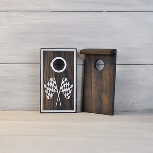 May include: Two wooden game boards with a chequered flag design. The board on the left has a hole in the centre and the board on the right has a rectangular opening.