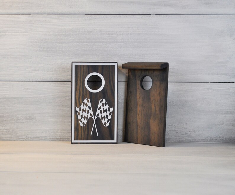 May include: Two wooden game boards with a chequered flag design. The board on the left has a hole in the centre and the board on the right has a rectangular opening.