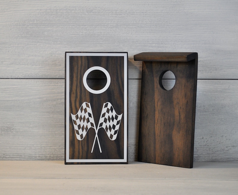 May include: Two wooden game boards featuring a chequered flag design and a circular hole. The boards are dark brown with a wood grain pattern.