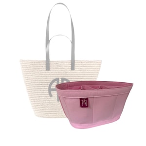 Könnte beinhalten: Ein rosa Filz-Taschenorganizer mit mehreren Fächern und einem kleinen Etikett mit den Buchstaben "A" und "A" in burgunder Farbe. Der Organizer ist so konzipiert, dass er in eine größere Strohtasche mit einem weißen und grauen Streifenmuster und einem silbernen Griff passt.