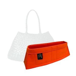 Puede incluir: Inserción de bolsa de fieltro naranja con múltiples compartimentos y un logotipo "A" negro. La inserción está diseñada para caber dentro de una bolsa de mano grande.