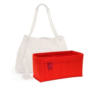 Peut inclure: Organiseur de sac en feutre rouge avec plusieurs compartiments et un petit logo sur le devant. L'organisateur est conçu pour s'adapter à l'intérieur d'un sac à main.