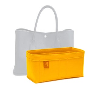 May include: A bright yellow felt handbag organizer with multiple compartments, shown in front of a light gray tote bag. The organizer has a rectangular shape and a small, brown label with a logo.